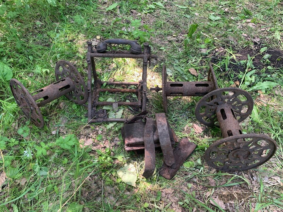 A dismantled field telephone cable-laying cart with cast spoked drum wheels and a handset, laid out on grass.