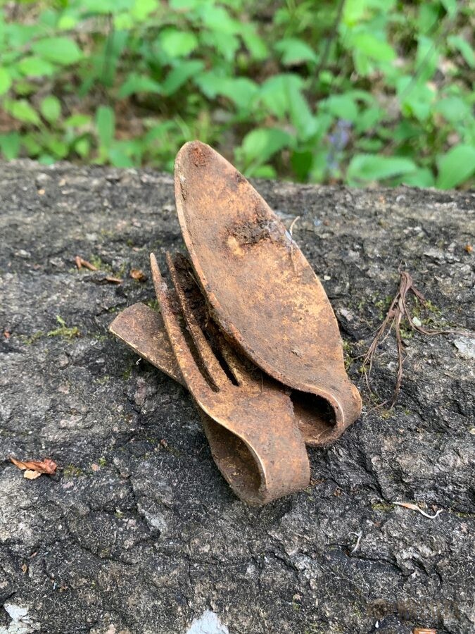 A rusted combination folding fork and spoon eating utensil standing on a lichen-covered stone.