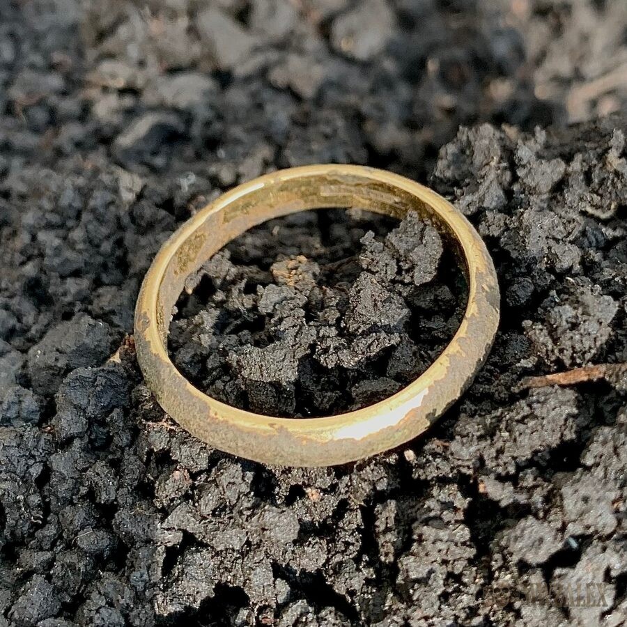 A plain gold-coloured ring resting on dark crumbly soil, photographed close up shortly after recovery.