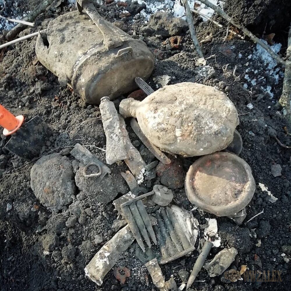 A group of excavated finds on snow-flecked soil including a canteen, a mess tin, an entrenching tool and pieces of cutlery.